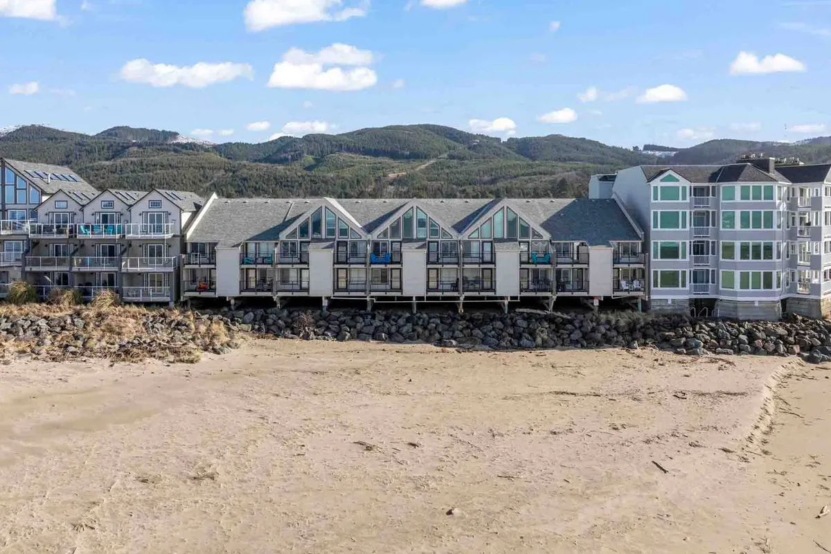 A scenic exterior image shows beachfront properties set against a backdrop of mountains, with inviting balconies and architectural features oriented toward the ocean. The scene suggests leisurely beach walks, sunset views, and intimate evenings spent together.