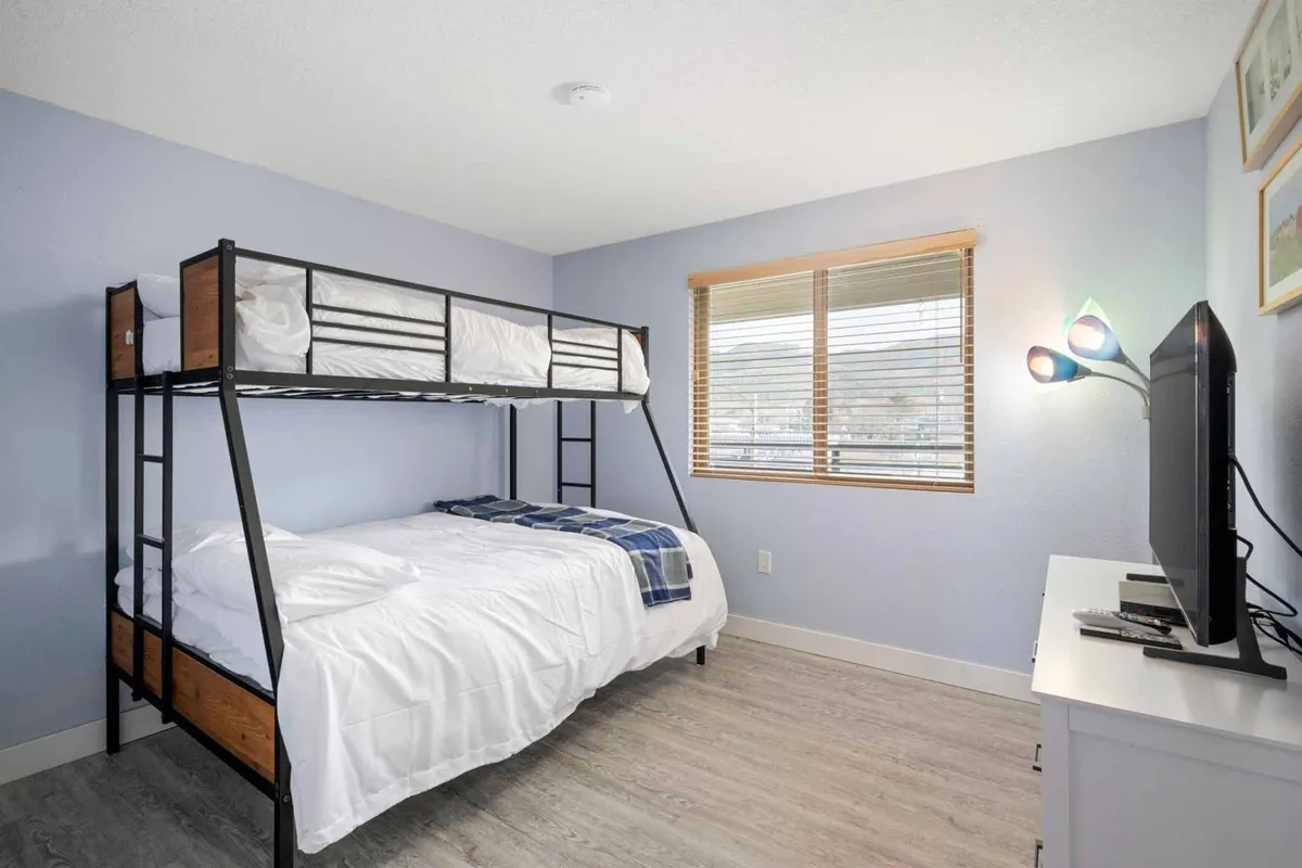 A cheerful bunk room with a sturdy bunk bed, a small television, and a window that brings in natural light. The space feels fun and cozy, ideal for children or friends, and promises flexibility for families.