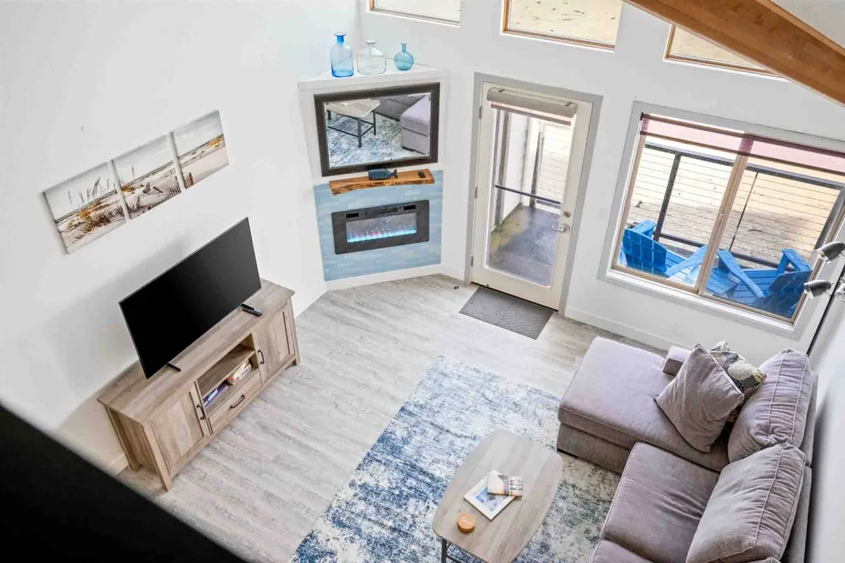 A spacious, comfortable living area with a large sofa, television, fireplace, coffee table, and expansive windows that offer views toward the outdoors. The arrangement encourages group gatherings, relaxation, and enjoying the natural light and scenery beyond the windows.