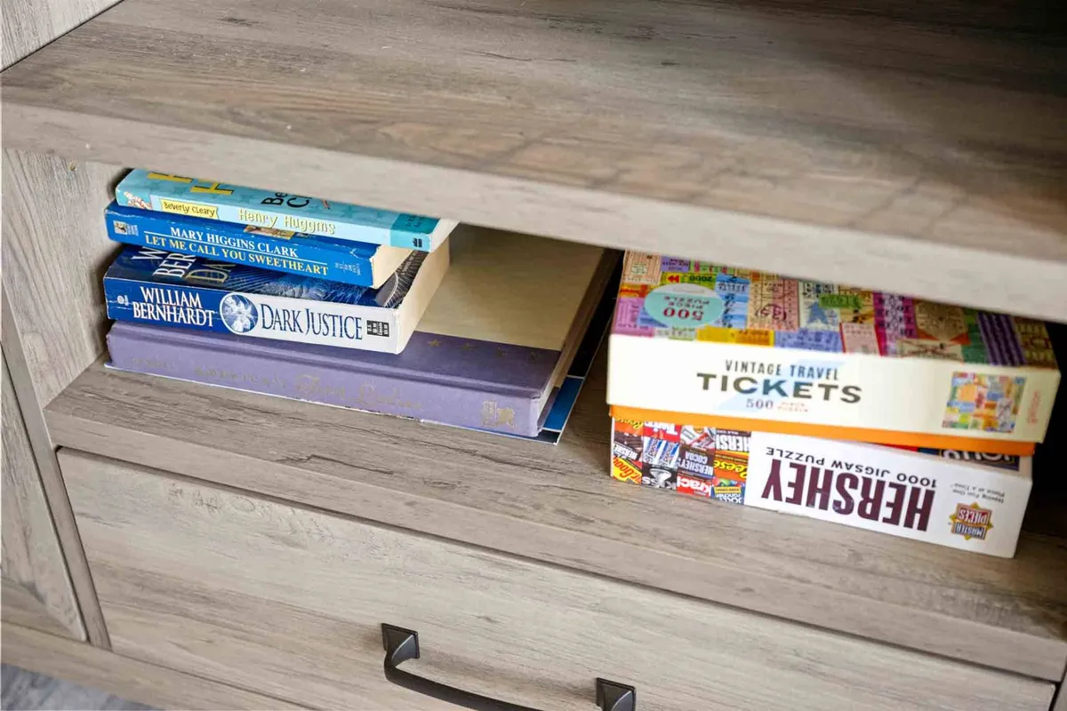 A welcoming nook with a small collection of books and puzzles organized in a drawer, suggesting a restful spot for reading or engaging your mind. The scene is intimate, warm, and encourages quiet, solo leisure time.
