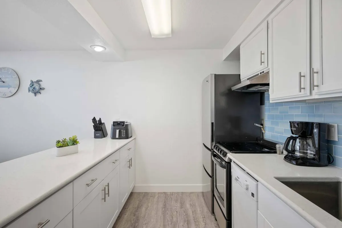 A modern kitchen scene showcasing white cabinetry, stainless steel appliances, a vibrant blue backsplash, and a countertop adorned with a decorative plant. The space exudes freshness, functionality, and is perfect for culinary adventures or coffee mornings.